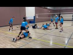 a group of people in blue shirts playing volleyball on a gym floor with one person laying on the ground