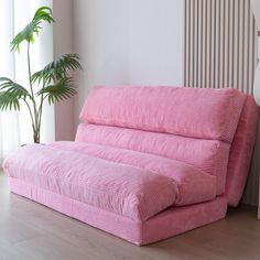 a pink couch sitting on top of a hard wood floor next to a potted plant