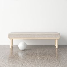 a white ball sitting on top of a floor next to a wooden bench and wall