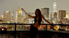 a woman standing on top of a roof in front of a cityscape at night