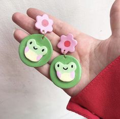 a hand holding two green and pink earrings with flowers on it's ear ends