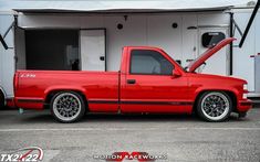 a red pick up truck parked in a parking lot next to a white trailer with the door open