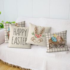 three pillows on a white couch with the words happy easter printed on one side and an egg in the other