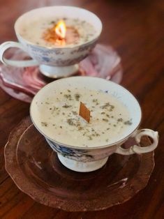 two cups filled with soup sitting on top of a wooden table next to a lit candle