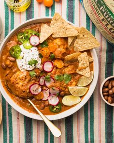 a white bowl filled with chicken chili and tortilla chips on top of a striped table cloth