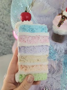 a hand holding a piece of cake with frosting and cherries on top in front of a christmas tree