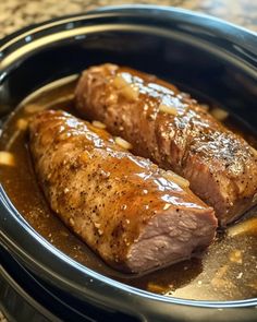 two pieces of meat in a slow cooker with sauce on the top and sides