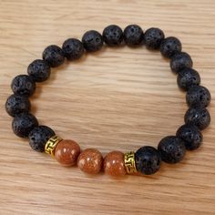 The bracelet contains two stones that are vital to our wellbeing: Goldstone and Lava Stone. The sparkles of Goldstone are symbolic of light that can always be found in the darkness. It deflects unwanted energies and is highly regarded in the spirit realm as a protective mineral. Lava Stone is a grounding stone that strengthens the connection to Mother Earth. A calming stone, it is instrumental in dissipating anger. It promotes positive changes where needed in behavioral issues. Our Brown Goldsto Brown Natural Stones Bracelet For Meditation, Black Spiritual Lava Stone Jewelry, Hand-strung Lava Stone Bracelet For Gift, Casual Hand-strung Lava Stone Beaded Bracelets, Spirit Realm, Hand-strung Lava Stone Bracelets, Positive Changes, Calming Stones, In The Darkness