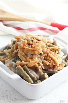 a white dish filled with green beans covered in toppings