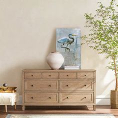 a white vase sitting on top of a wooden dresser next to a painting and a potted plant