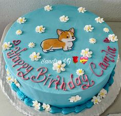 a blue birthday cake with a corgi on top and happy birthday written in pink