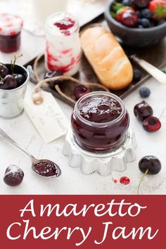 there is a jar of cherry jam on the table with cherries and bread in the background