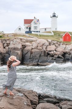 a woman standing on top of a rock next to the ocean with a lighthouse in the background