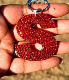 a hand holding a red keychain with the letter s in it's center