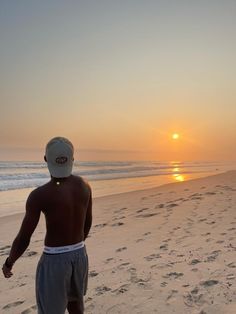 a man standing on top of a sandy beach next to the ocean at sun set