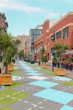 an empty city street with potted plants on the sidewalk and people sitting at tables