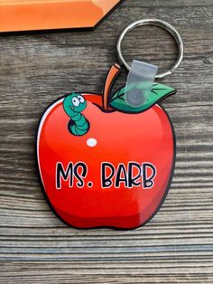 a red apple shaped keychain with the words ms bard on it and a worm sticking out of it