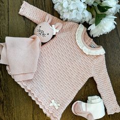 a pink knitted sweater and booties on a wooden floor next to white flowers