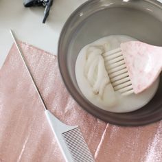 a brush and comb sitting in a bowl on a pink table cloth next to scissors