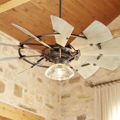 a ceiling fan that is hanging from the ceiling in a room with stone walls and wood beams