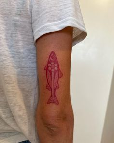 a person with a red fish tattoo on their arm and the word love is written in pink ink