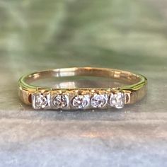 a yellow gold ring with five diamonds on it's side, sitting on a stone surface