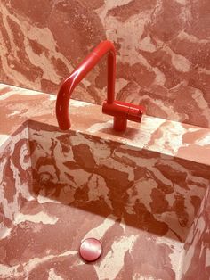 a bathroom sink with red faucet and marble walls