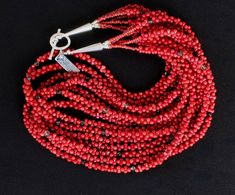 This elegant Necklace showcases 7 strands of Bamboo Coral Peanuts. The "Peanut" designation refers to the cut; each piece is shaped with a pinched center and wider ends. This allows the Coral to interlock, adding texture and visual interest to the design. The Bamboo Coral is a striking coral-red and polished to a glossy sheen. We've paired the Coral with 2 styles of Czech Glass, including Picasso red 4mm Faceted Ovals, and 4mm champagne-hued Crystal Bicones. These elements contribute color depth Multi-strand Red Coral Jewelry Gift, Red Hand-strung Multi-strand Jewelry, Unique Red Multi-strand Jewelry, Handmade Multi-strand Red Coral Jewelry, Artisan Multi-strand Red Beads, Bamboo Coral, Southwest Design, Red Tote, The Coral