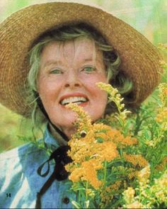 an older woman wearing a straw hat and holding yellow flowers in her hands while smiling