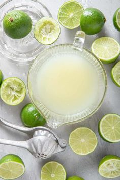 limes surrounding a pitcher of lemonade on a table