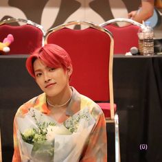 a woman sitting in a chair with flowers on her lap and wearing an orange tie dye shirt