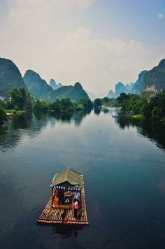 a small raft floating on top of a river surrounded by mountains and greenery in the distance