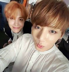 two young men are posing for a selfie in an office setting, one is wearing a white shirt and the other has red hair