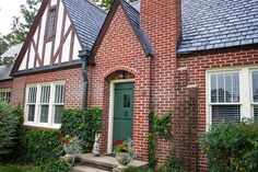 a red brick house with green door and windows