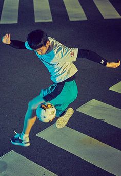 a young man riding a skateboard down a street next to a cross walk with his foot in the air