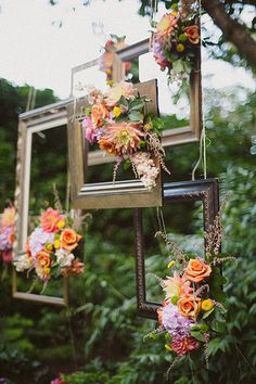 an arrangement of flowers is hanging from a frame in the woods with greenery behind it