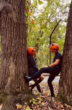 two people wearing orange helmets sitting in the middle of a tree with leaves on the ground