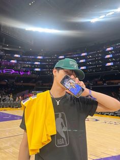 a young man wearing a green hat and holding a cell phone to his ear while standing on a basketball court