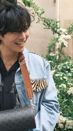 a young man is smiling and holding a purse in his hand while wearing a denim jacket