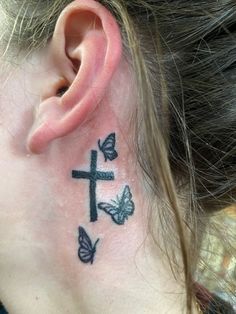 a close up of a person with a cross and butterflies tattoo on their behind the ear