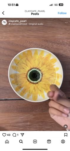 someone is holding up a yellow flower on a white plate with black center in the middle