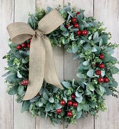 a christmas wreath with berries and greenery hanging on a wooden wall next to a bow