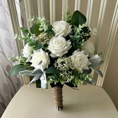 a bouquet of white roses and greenery sits on a table in front of a curtain