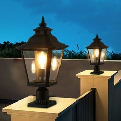 two lamps on top of a wall next to each other in front of a fence