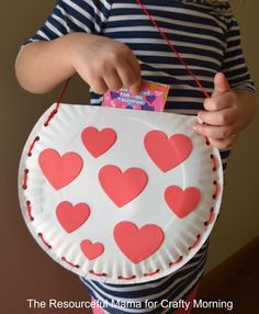 a child holding a paper plate with hearts on it and a card in the other hand