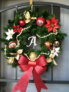 a christmas wreath hanging on the front door with red ribbon and poinsettis