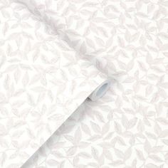 a white wallpaper with leaves on it and a roll of paper next to it