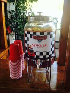 a large glass jar sitting on top of a wooden table next to two red cups