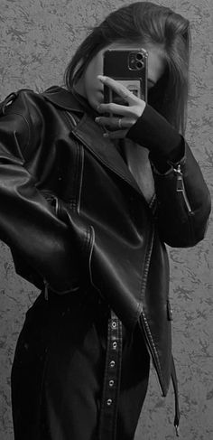 black and white photograph of a woman taking a selfie with her cell phone while wearing a leather jacket