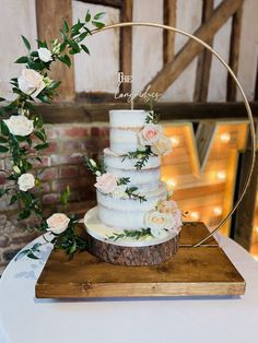 a wedding cake with flowers and greenery sits on a wooden stand in front of a brick wall